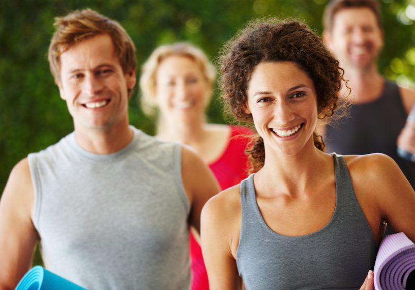 healthy weight challenges Group of people in gym gear holding exercise mats with a smiling ethnic girl and male in the front